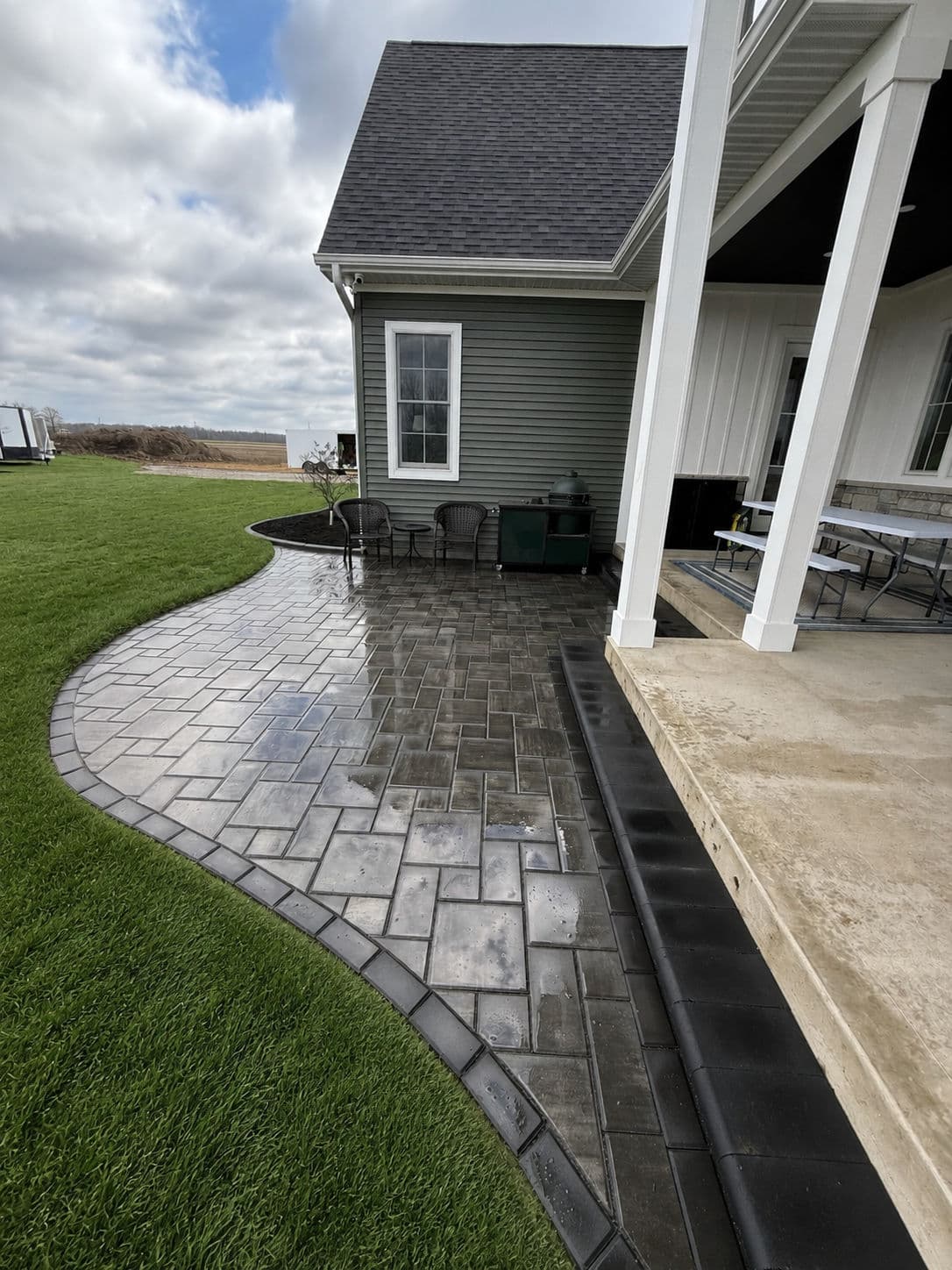 Curved paver patio and lawn beside a modern home with grey siding and outdoor seating.