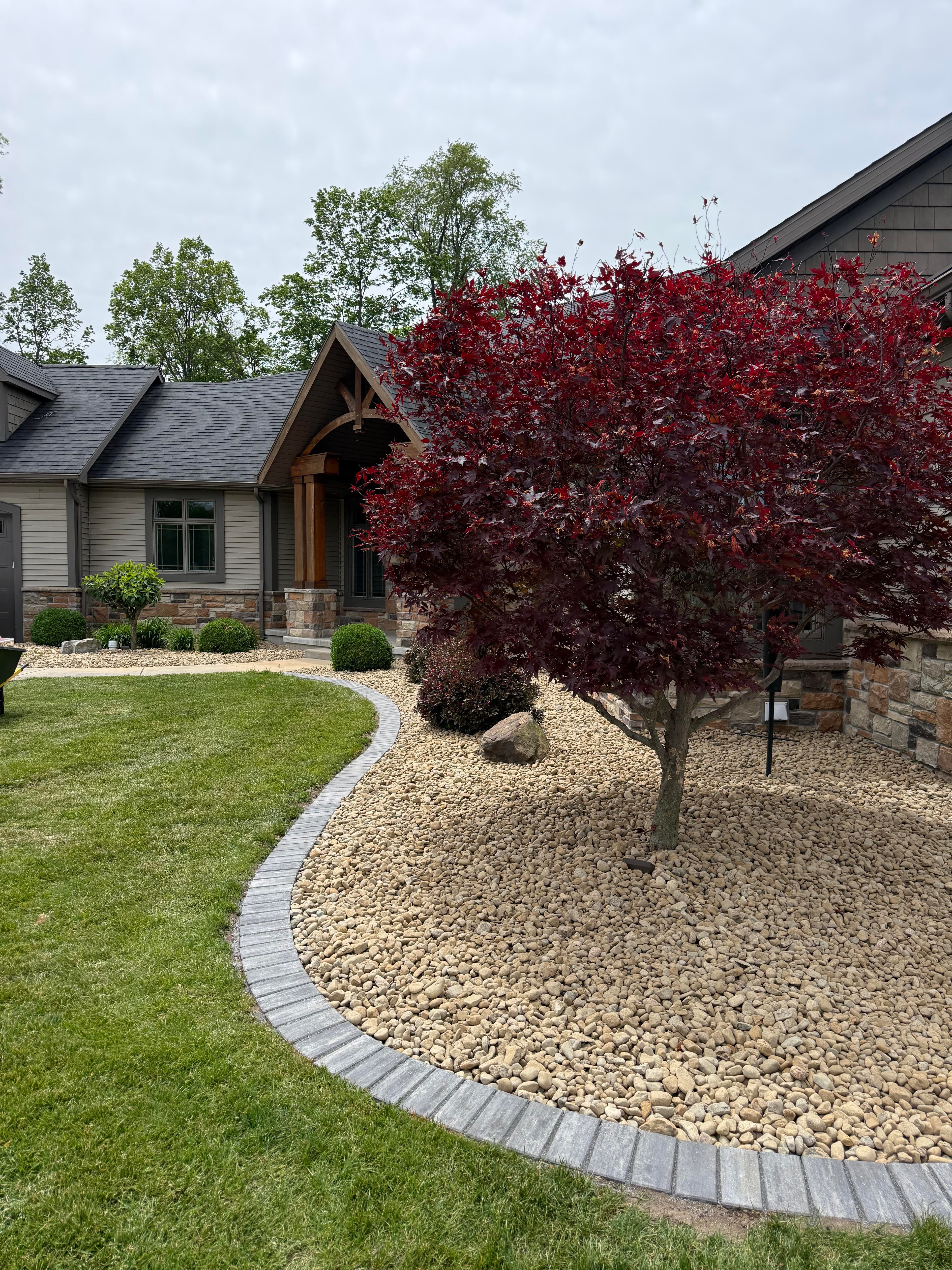 Landscape design featuring a red maple tree, stone pathway, and a modern home exterior.
