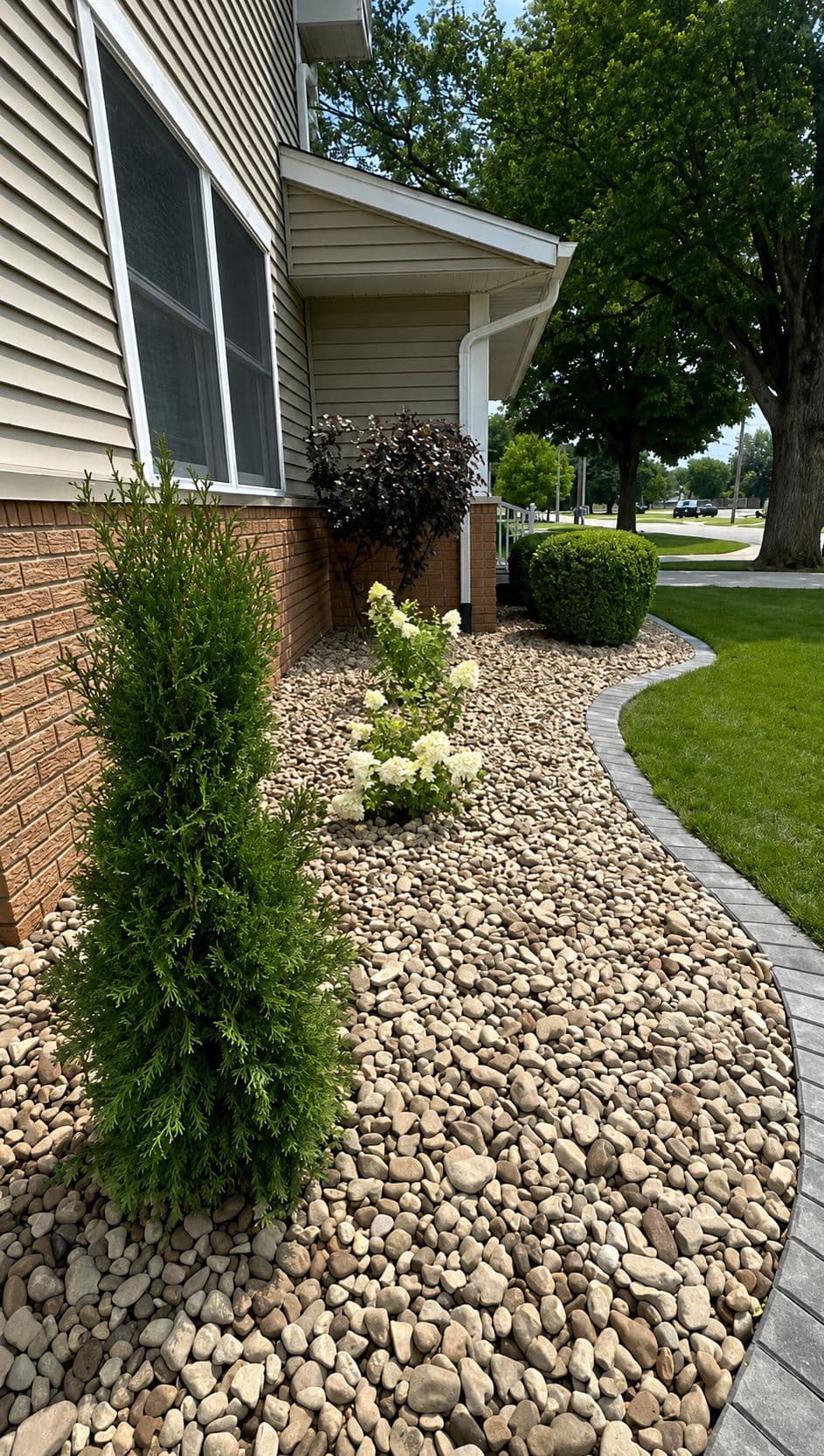 Landscaped garden featuring stones, shrubs, and flowers along a house exterior.