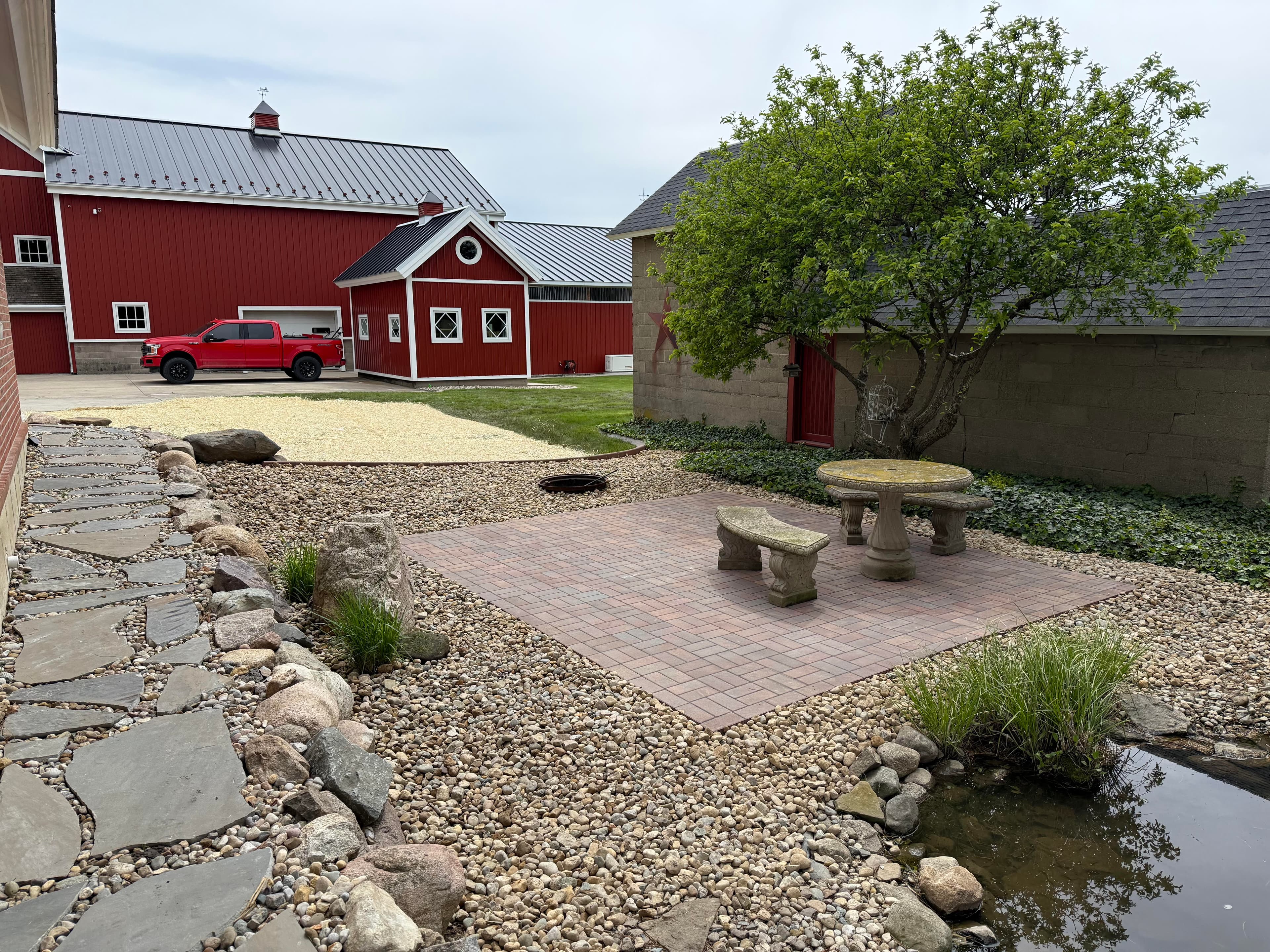 Red barn and truck with outdoor seating area and stone path in scenic landscape.