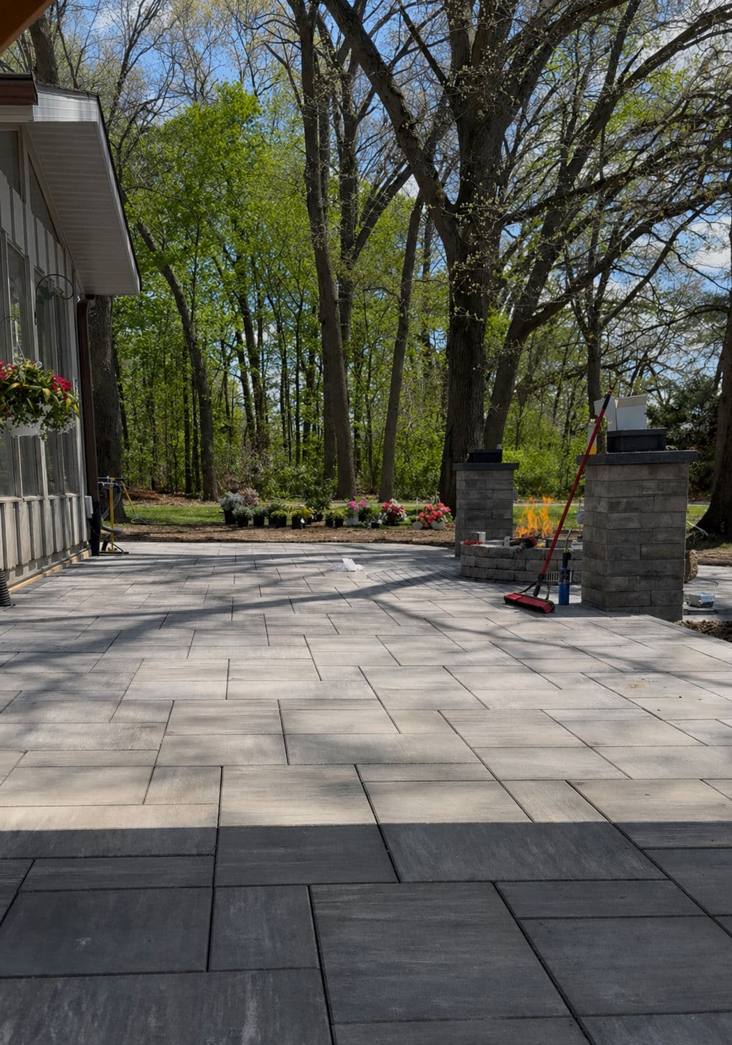Patio area with gray pavers, green trees, and flower beds in a serene outdoor setting.