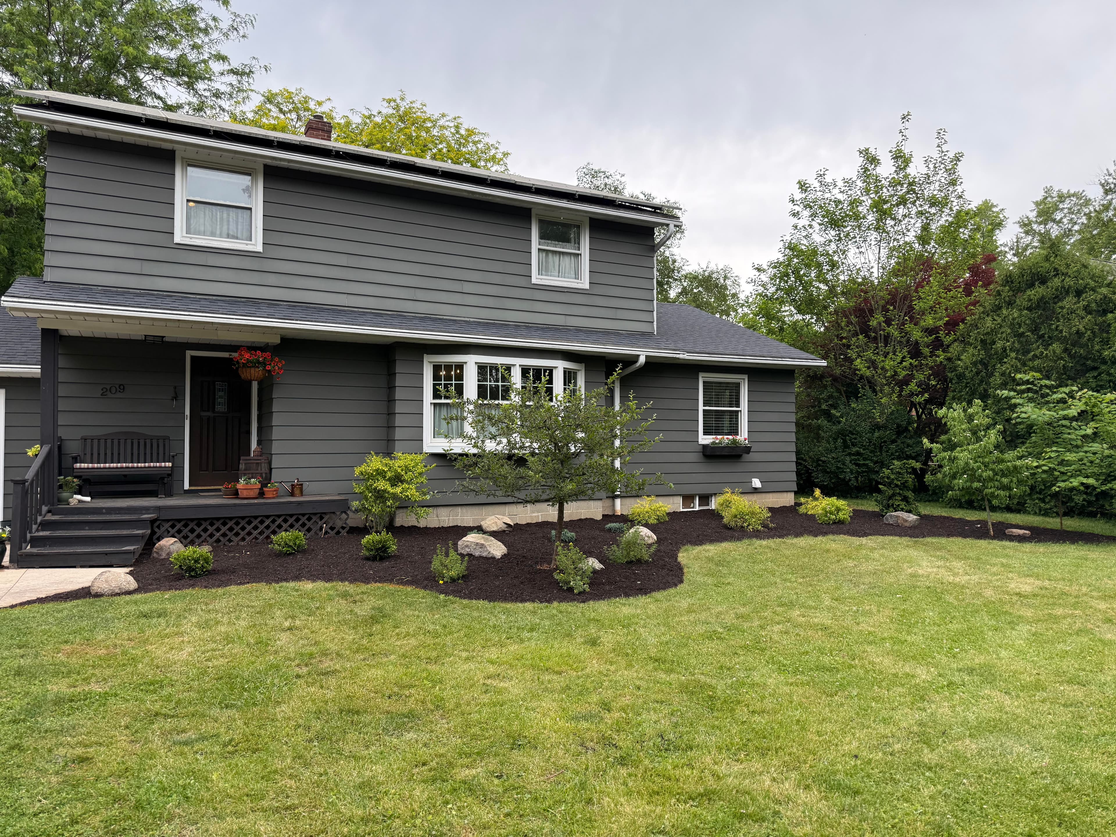 Gray two-story house with manicured lawn, flower pots, and landscaping features.