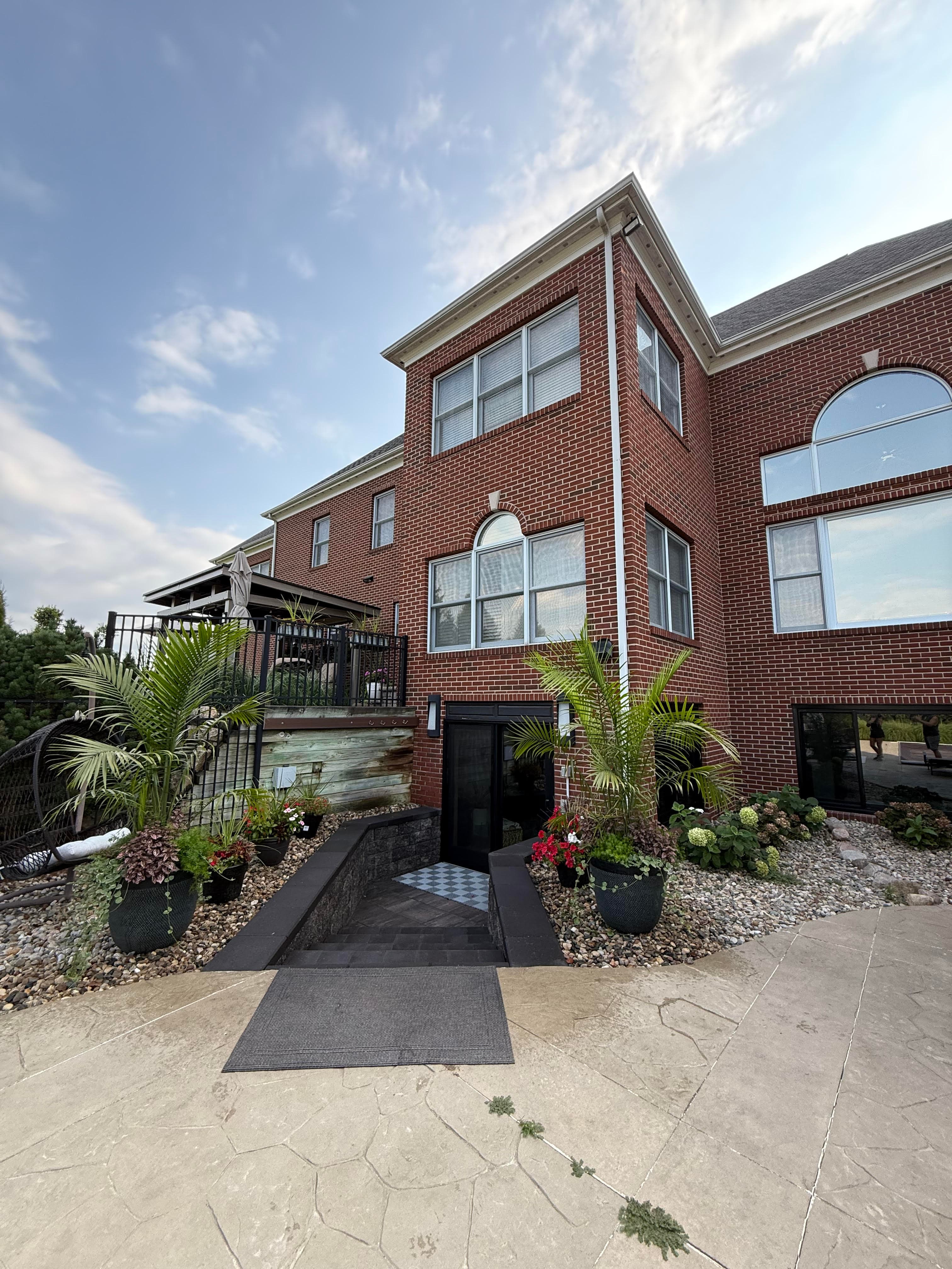 Modern brick house entrance with tropical plants and landscaped pathway, under a blue sky.