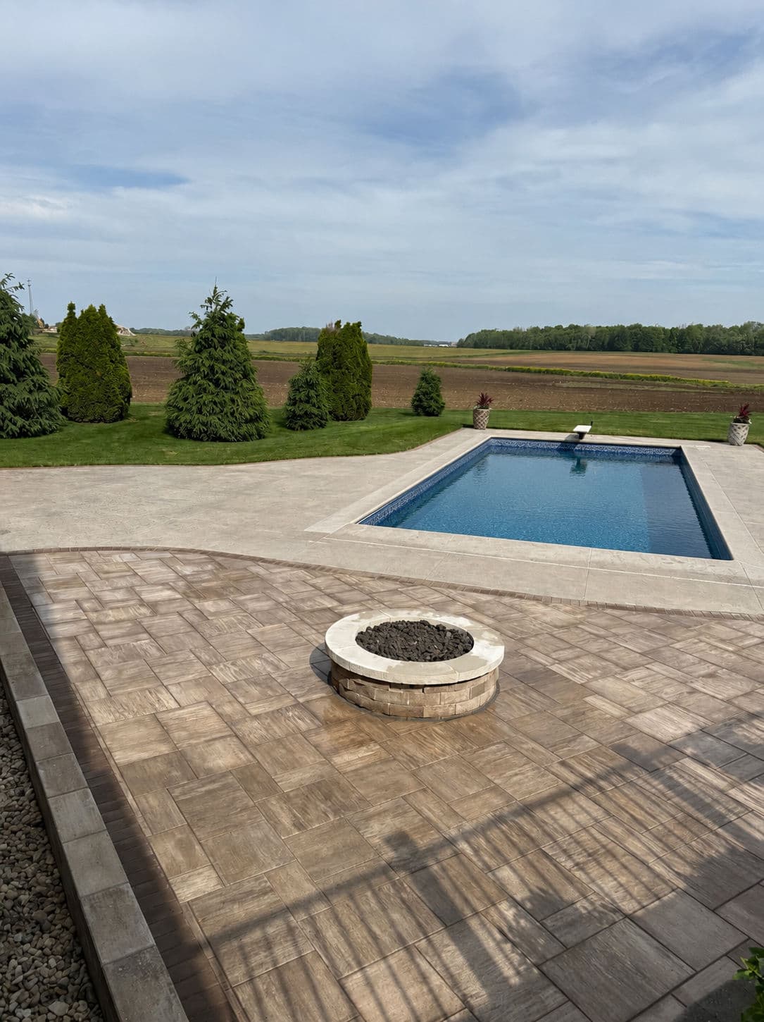 Backyard oasis featuring a swimming pool, fire pit, and landscaped greenery under a clear sky.