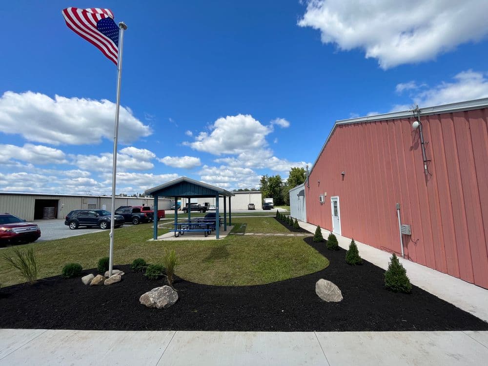 American flag beside a gazebo in a landscaped area with clouds in a blue sky.