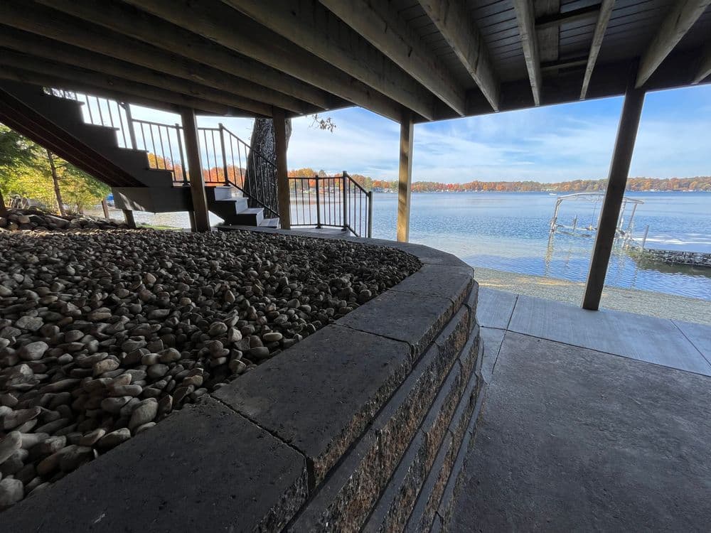 Scenic lakeside view from under a wooden deck with stone landscaping and staircase.