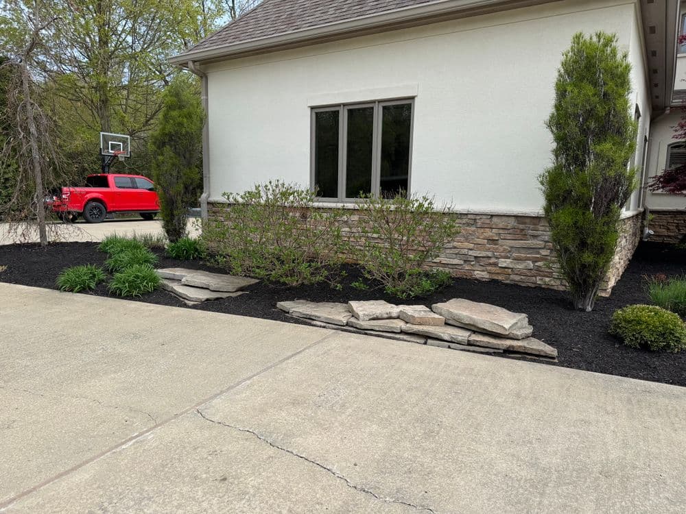 Landscaped home exterior with stone accents, greenery, and a red vehicle parked nearby.