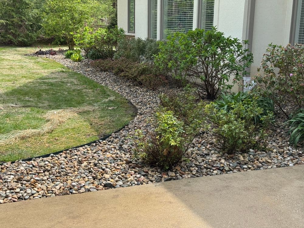 Landscaped garden path with decorative rocks, shrubs, and greenery near a modern home.