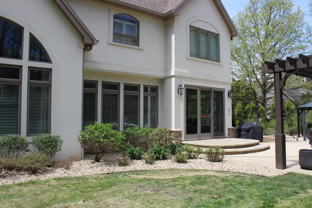 Modern two-story home exterior with stone accents, lush landscaping, and patio area.