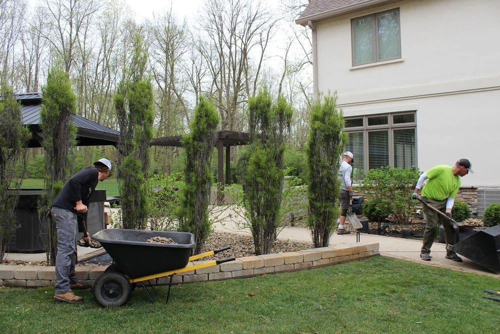 Landscape workers using wheelbarrows to maintain a residential garden near a house.