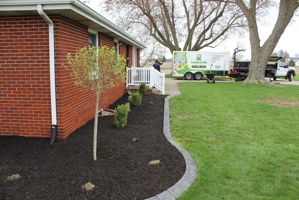 Front yard landscaping with fresh mulch, small trees, and a landscaping truck in the background.