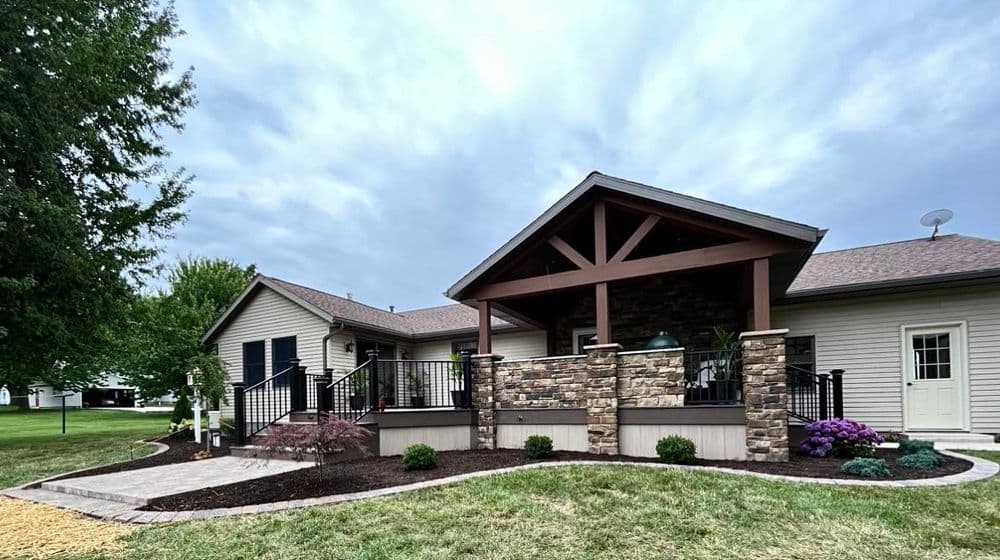 Modern home exterior featuring a stone porch, landscaped yard, and cloudy sky backdrop.