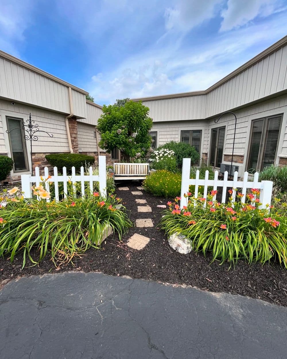 Charming courtyard with a white picket fence, flower beds, and a seating area under a tree.
