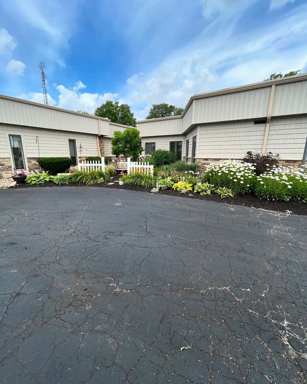 Well-landscaped entrance with flowers and shrubs beside a paved driveway under a blue sky.