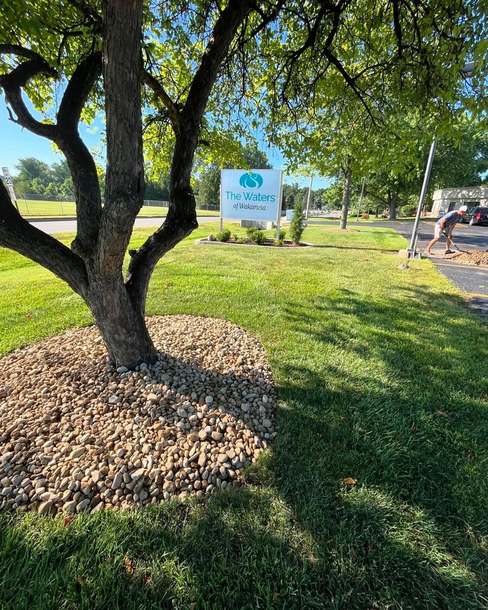 Sign for The Waters of Wellington surrounded by lush greenery and a tree.